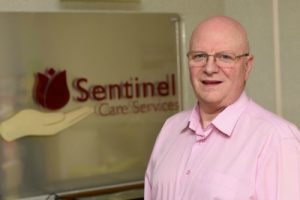 Steve Harris standing next to the Sentinel Care Services sign.